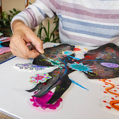 A person painting colourful details onto artwork at a table
