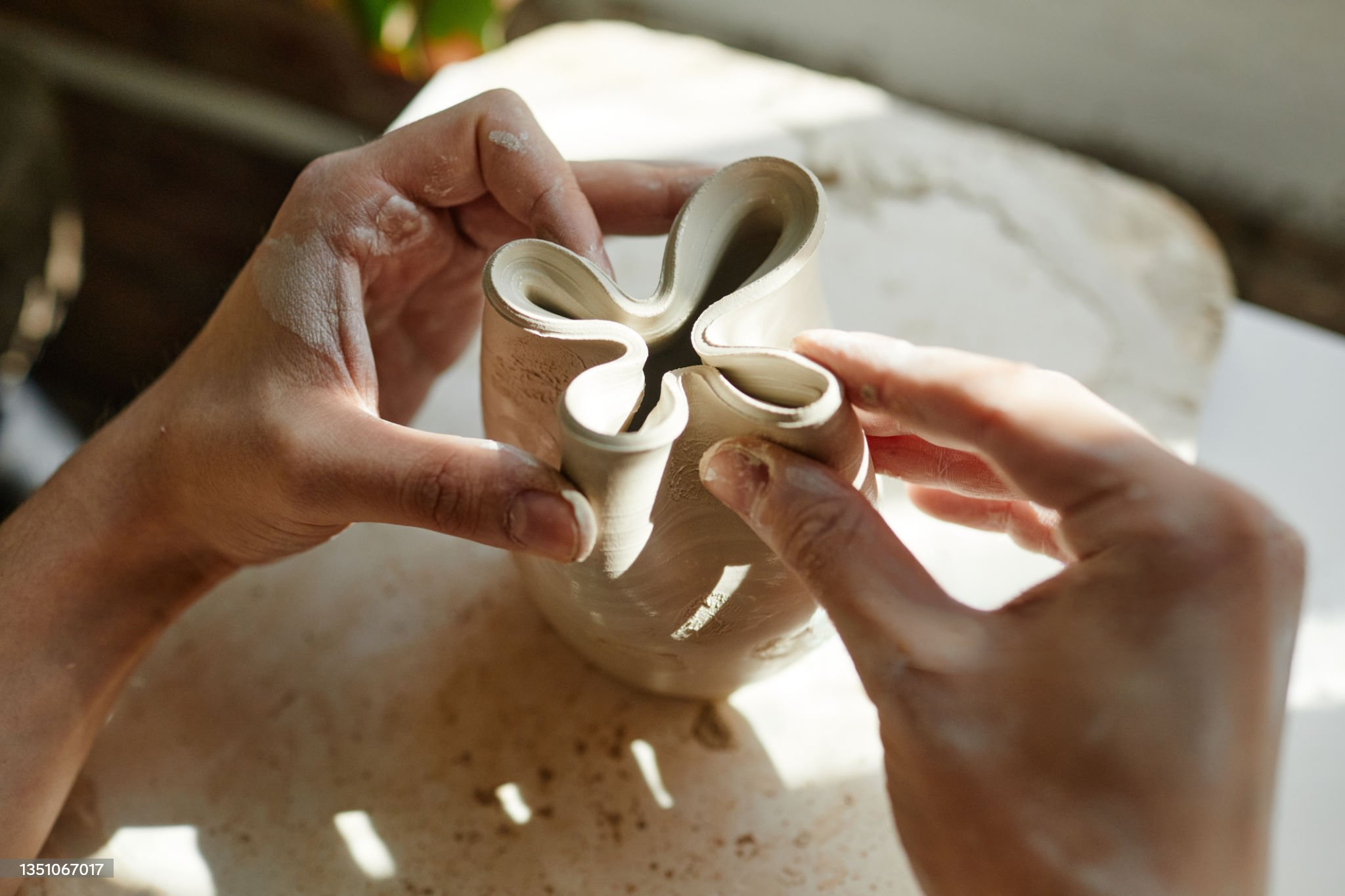 Hands gently shaping the rim of a clay vessel